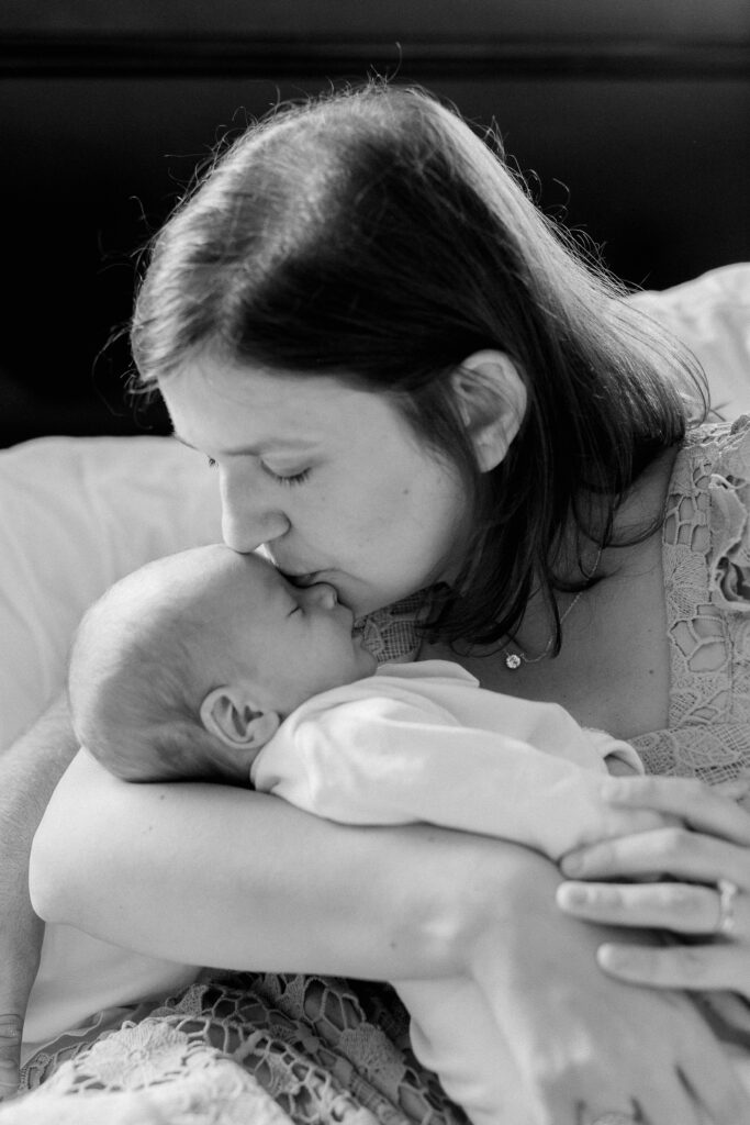 Black and white image of a mother kissing her newborn baby on the forehead