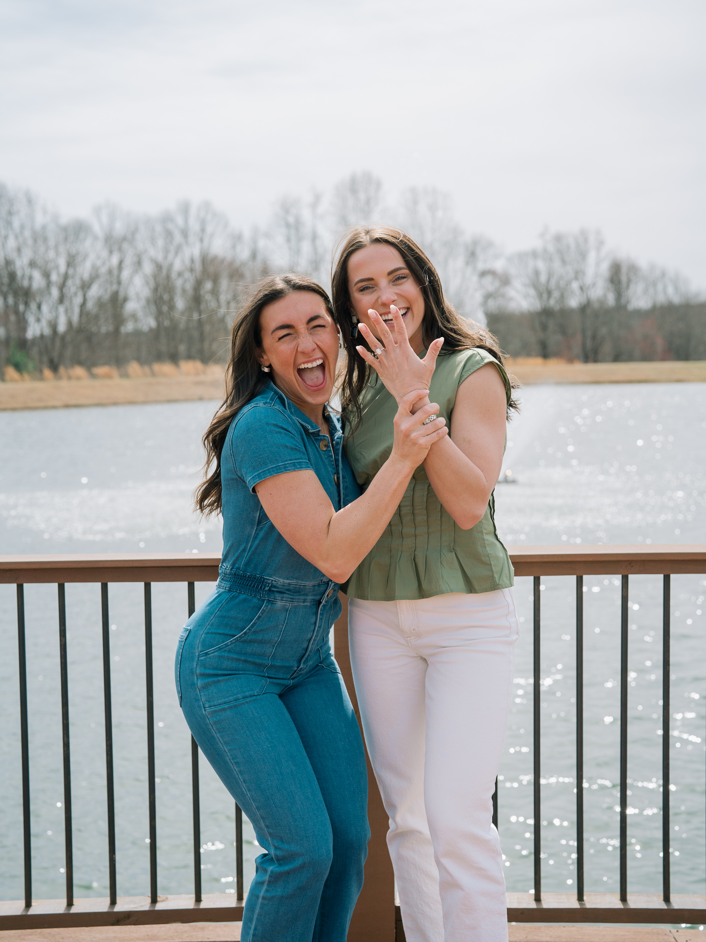 A joyful moment as a women grabs her best friend's hand to flash her new engagement ring off to the camera. Both women have huge smiles.