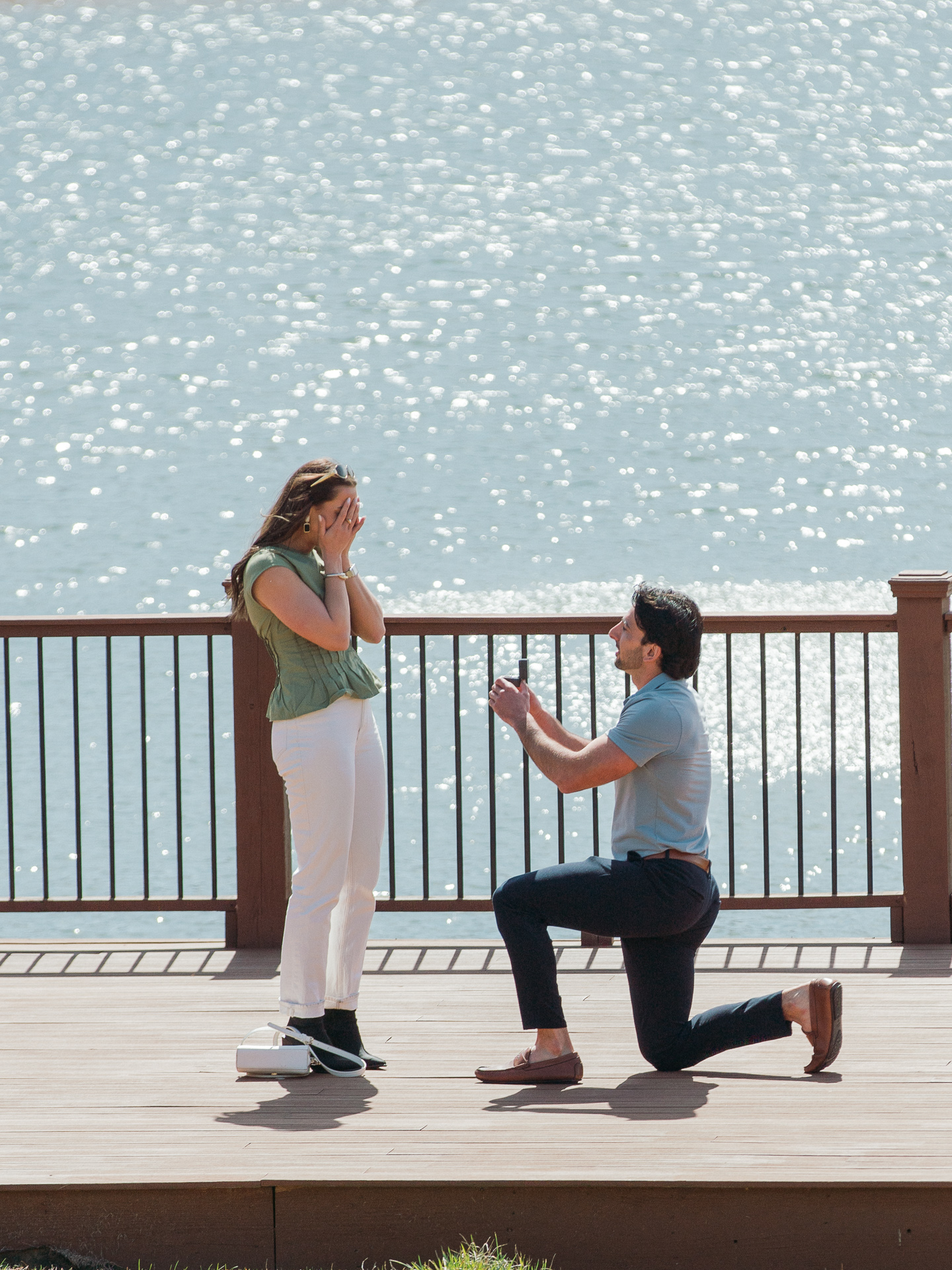 An emotional moment as a women covers her face as her boyfriend kneels with a ring box proposing to her in front of a picturesque pond at Montaluce Winery.