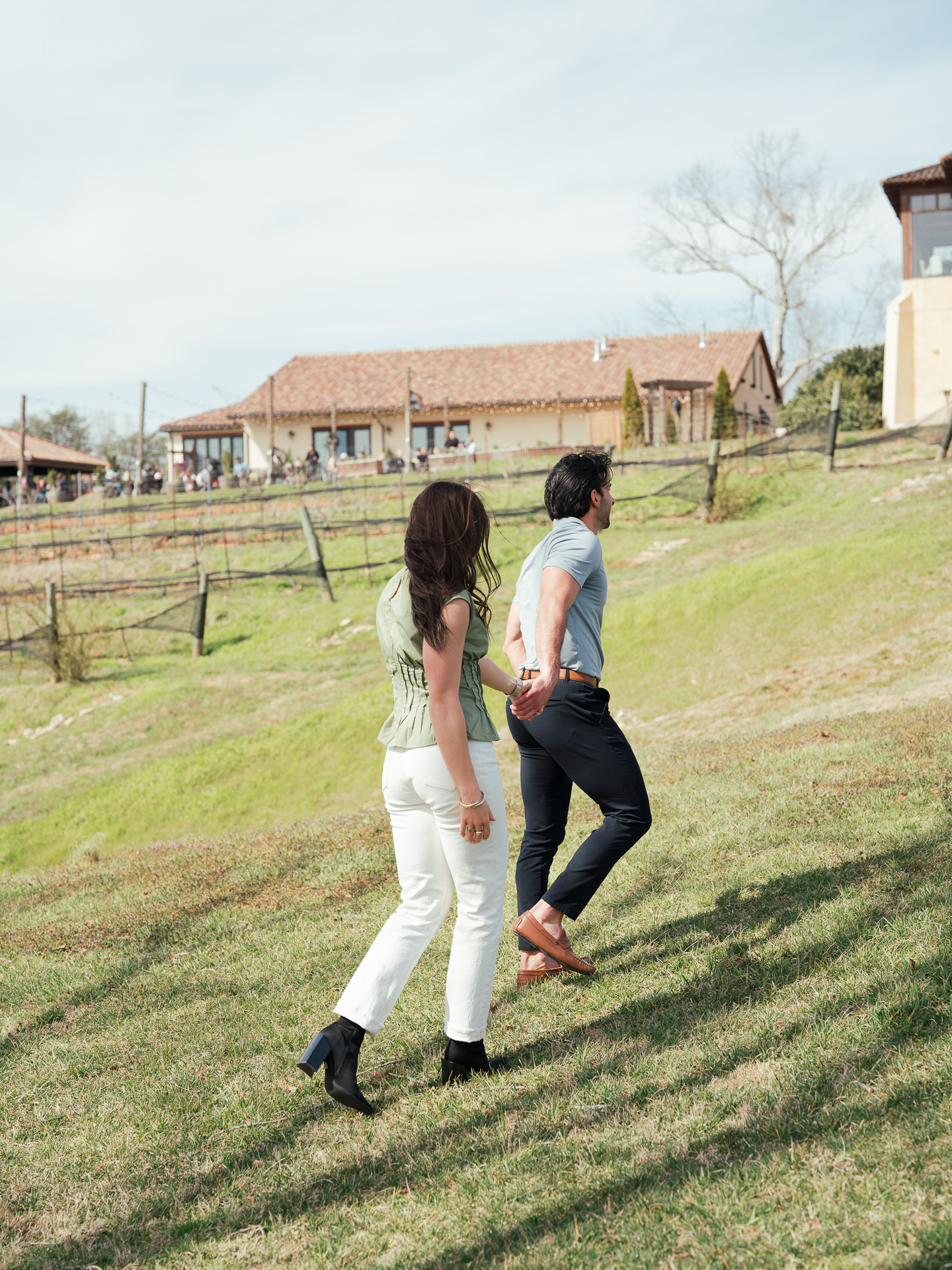 A candid shot of a couple walking away from the camera, hand in hand up the hill to Montaluce Winery.